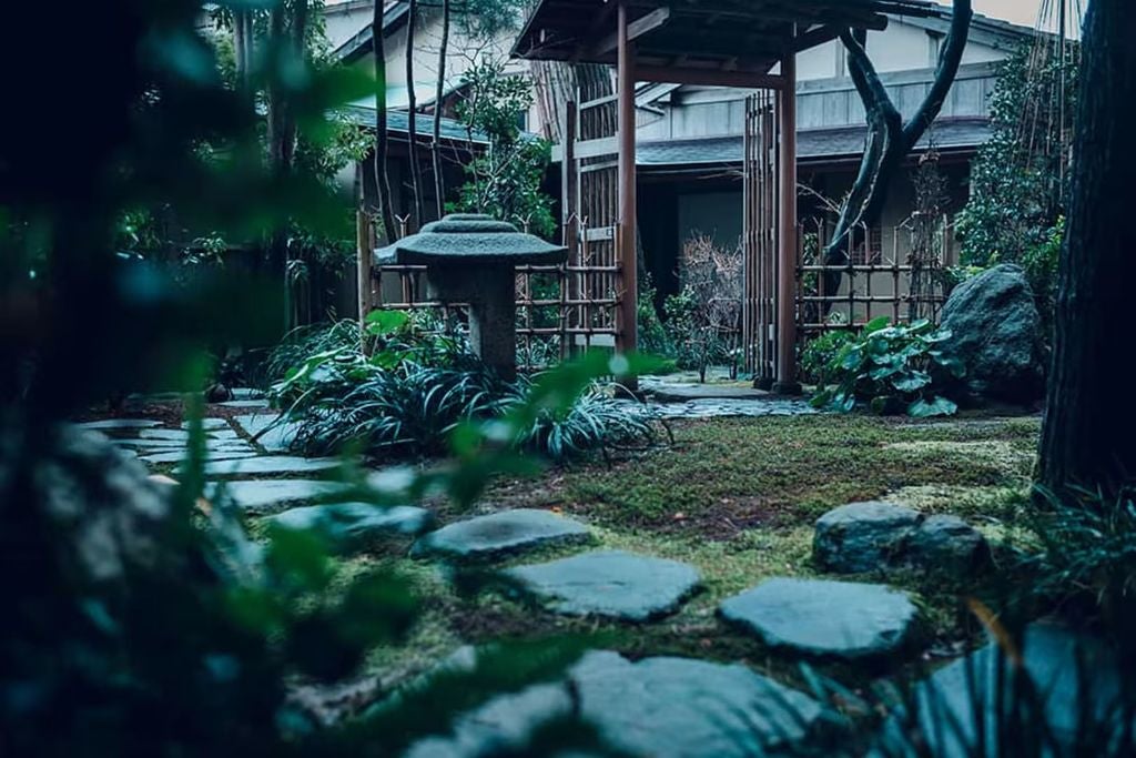 Traditional Japanese ryokan with wooden architecture featuring illuminated lanterns, overlooking tranquil waters at golden hour