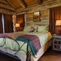 Rustic lodge room with wooden furnishings, large windows overlooking scenic mountain landscape, plush bedding, and warm earthy color palette in rural United States.