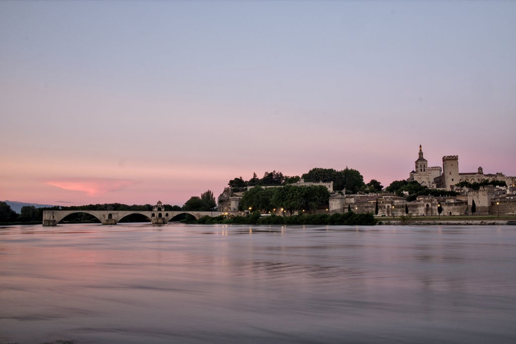 Historic Palais des Papes dominates Avignon skyline at sunset, with elegant stone architecture and Gothic spires against warm sky