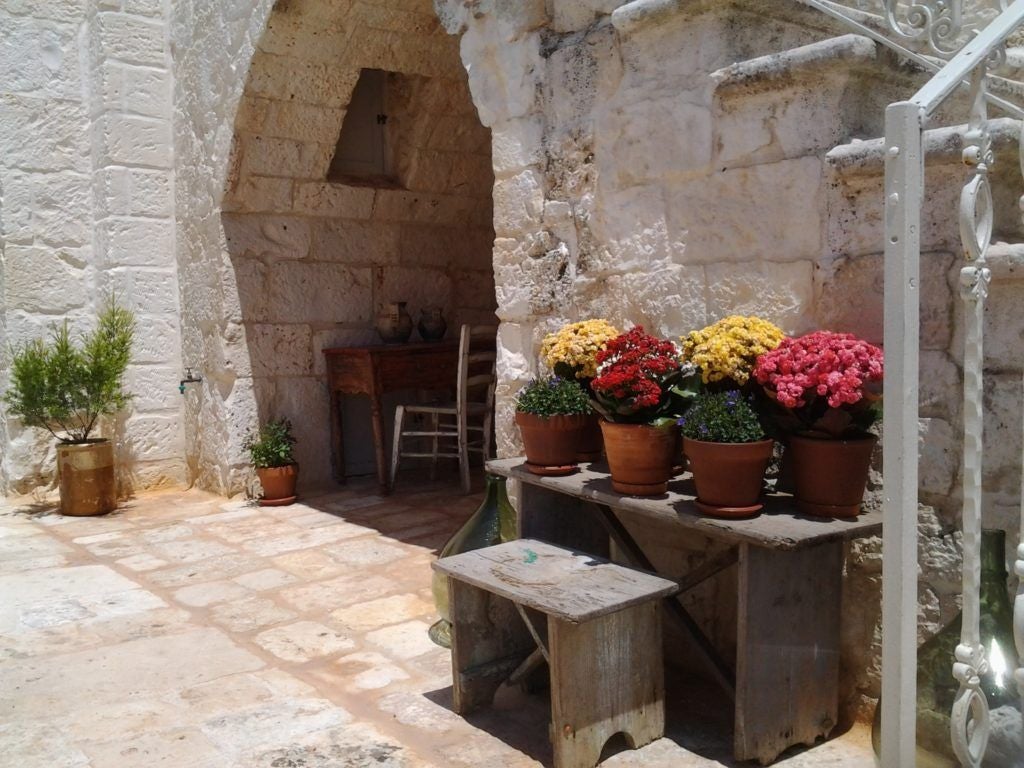 Rustic stone farmhouse nestled in Puglia's countryside, with warm golden light highlighting traditional architecture and lush olive grove surroundings.