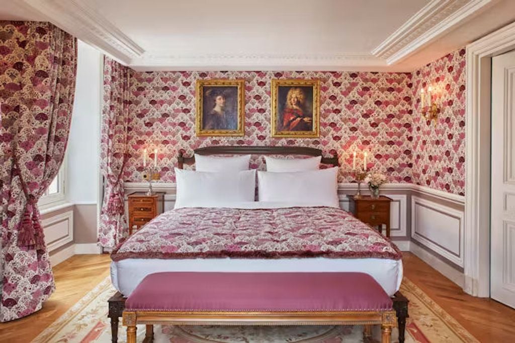 Opulent French château hotel room with ornate gold details, period furniture, crystal chandelier and floor-to-ceiling windows in warm light