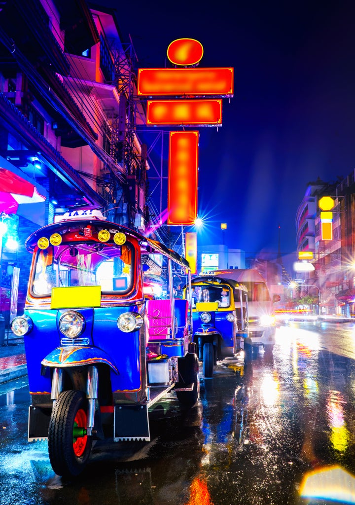 Three illuminated tuk tuks parked at night outside an upscale Bangkok restaurant, red lanterns casting a warm glow on diners