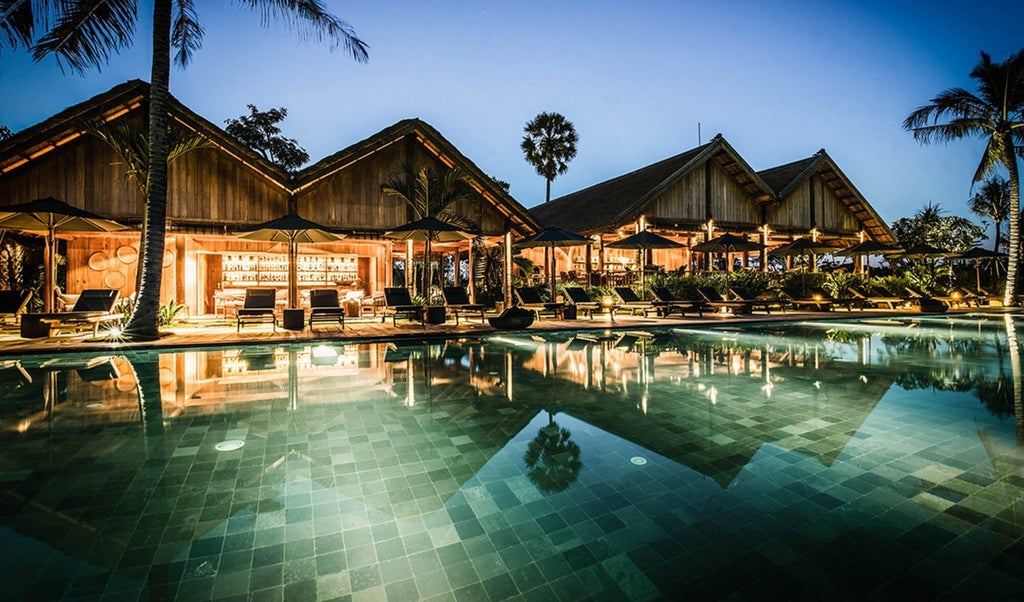 Luxurious Khmer-style wooden villa with private terrace overlooking lush rice paddies and tropical gardens at sunset in Cambodia