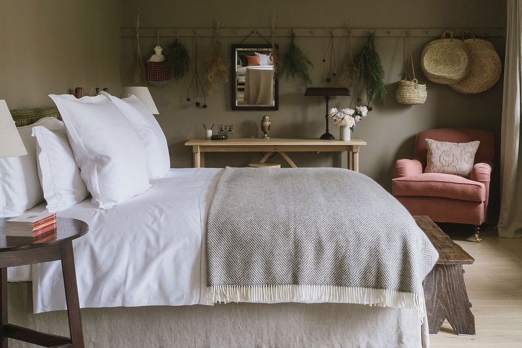 Elegant master bedroom at Heckfield Place with soft neutral tones, rich wood furnishings, plush bedding, and expansive countryside views through large windows.