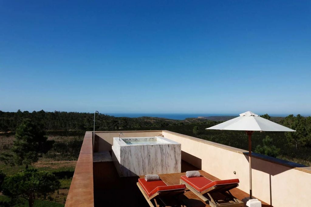 Luxurious beachfront hotel with white facade and glass balconies overlooking turquoise ocean waters and golden sand beach in Portugal