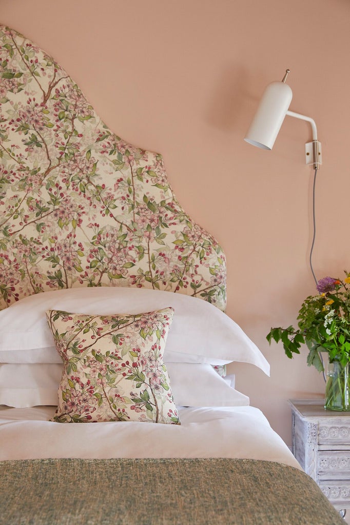 Elegant cottage suite bedroom with plush white bedding, rustic wooden furnishings, soft green thyme-inspired accents, and large garden-view window in UK countryside