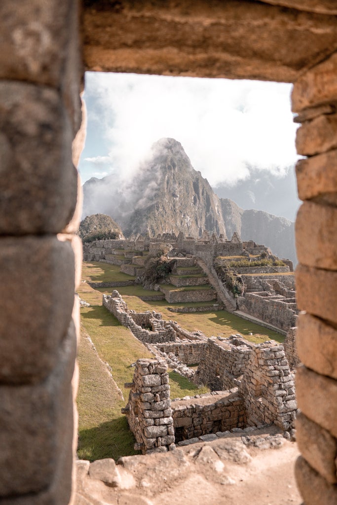 Iconic Machu Picchu citadel perched on misty mountain ridge, with lush green terraces and ancient stone architecture at sunrise