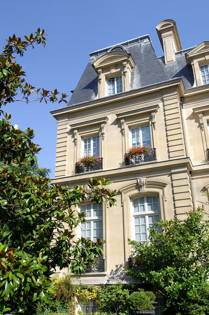 Ornate cream-colored Parisian mansion hotel with mansard roof, wrought-iron balconies and red-striped awnings set in manicured gardens