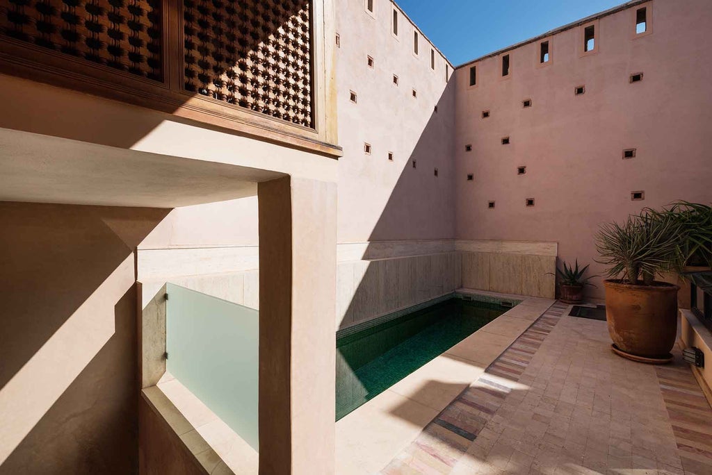 Ornate Moroccan riad courtyard with elegant archways, traditional tilework, and a tranquil fountain pool surrounded by potted plants and loungers