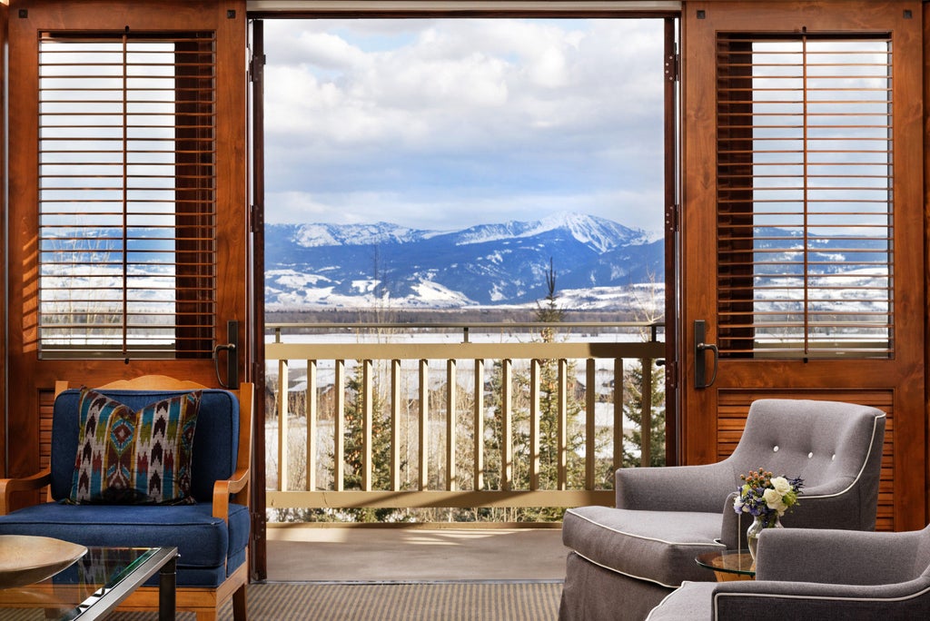 Snow-covered mountain peaks frame luxury ski-in resort with grand stone-and-timber facade, multiple balconies and outdoor fire pits