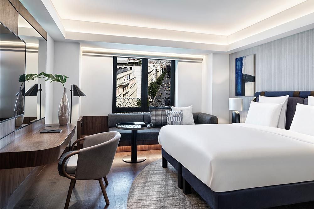 Elegant deluxe hotel room with king bed, contemporary decor, floor-to-ceiling windows overlooking Athens cityscape, marble bathroom