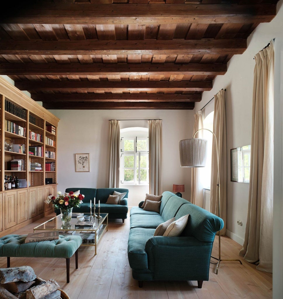 Rustic luxury corner barn suite at Bethlen Estates, featuring wooden beams, antique furnishings, and panoramic Transylvanian countryside views through large windows.