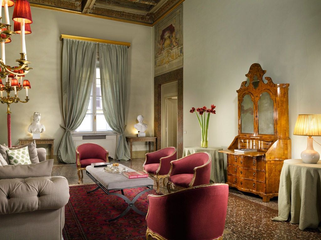 Historic Italian palazzo with ornate Renaissance architecture, elegant stone facade, arched windows, and lush green courtyard in soft afternoon light