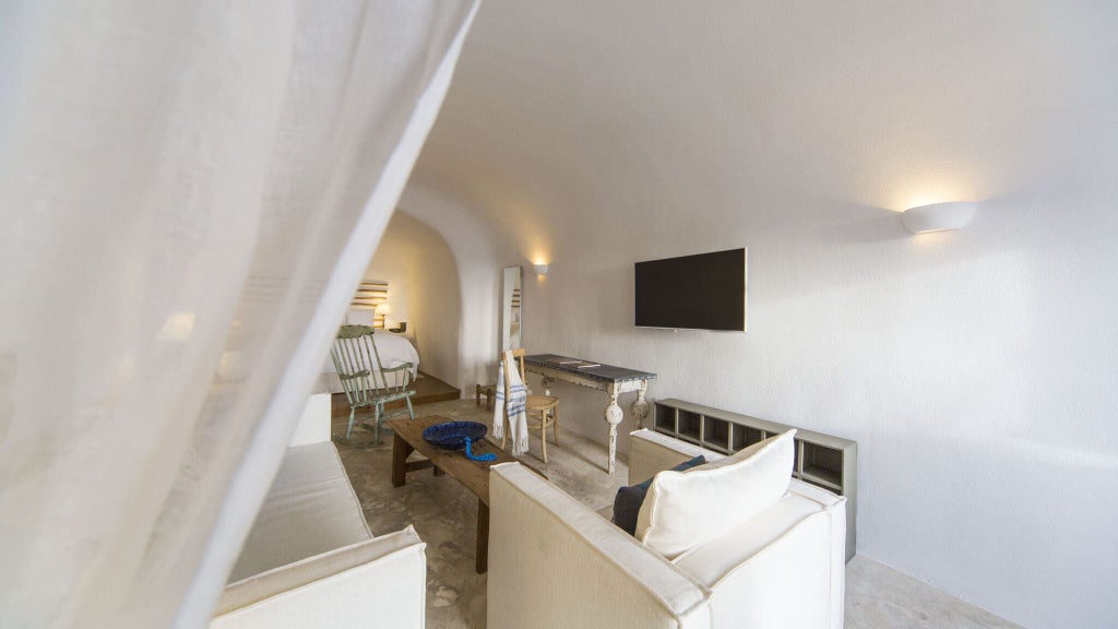 Luxurious white-washed cave suite with blue-domed ceiling, panoramic Aegean Sea view, and minimalist Cycladic design at Santorini boutique hotel