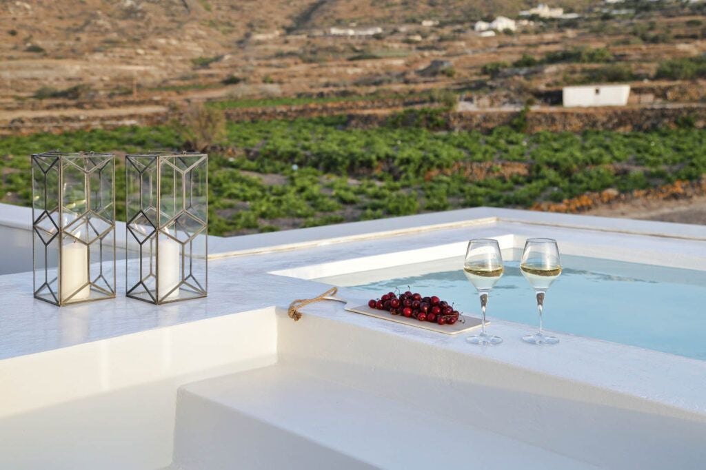 Luxurious whitewashed Greek villa with blue-domed roofs overlooking Aegean Sea, nestled among sun-drenched cliffs of a traditional Cycladic landscape