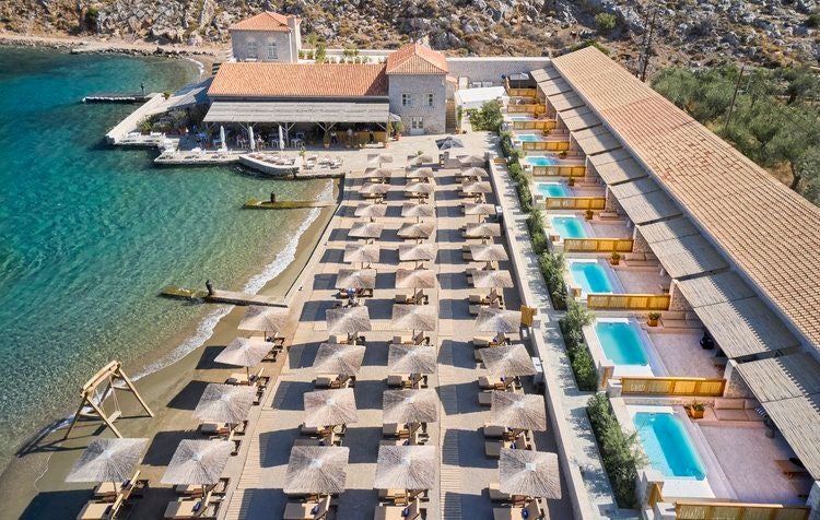 Pristine white resort buildings with private balconies cascade down a hillside to turquoise Mediterranean waters and a sandy beach in Rhodes