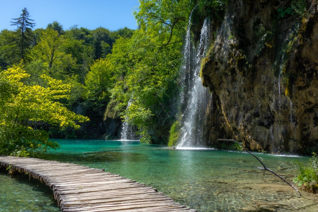 Group tours pristine Plitvice Lakes National Park in Croatia, with wooden boardwalks crossing turquoise waterfalls and lakes surrounded by forest