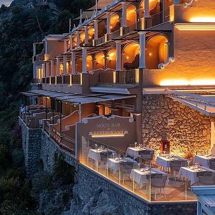 Luxurious coastal Hotel Luna with white stone facade, blue Mediterranean waters, and elegant terraced balconies overlooking scenic Italian shoreline at sunset