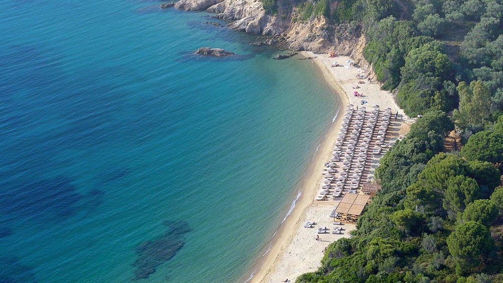 Luxurious beachfront hotel with white minimalist architecture, azure Aegean waters, and lush Mediterranean landscape at scenset resort