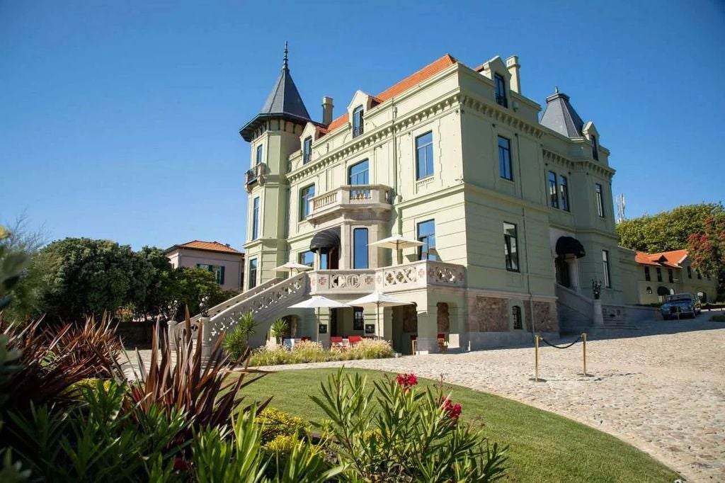 Elegant beachfront hotel in Porto featuring modern white architecture, floor-to-ceiling windows, and a manicured garden terrace overlooking the sea