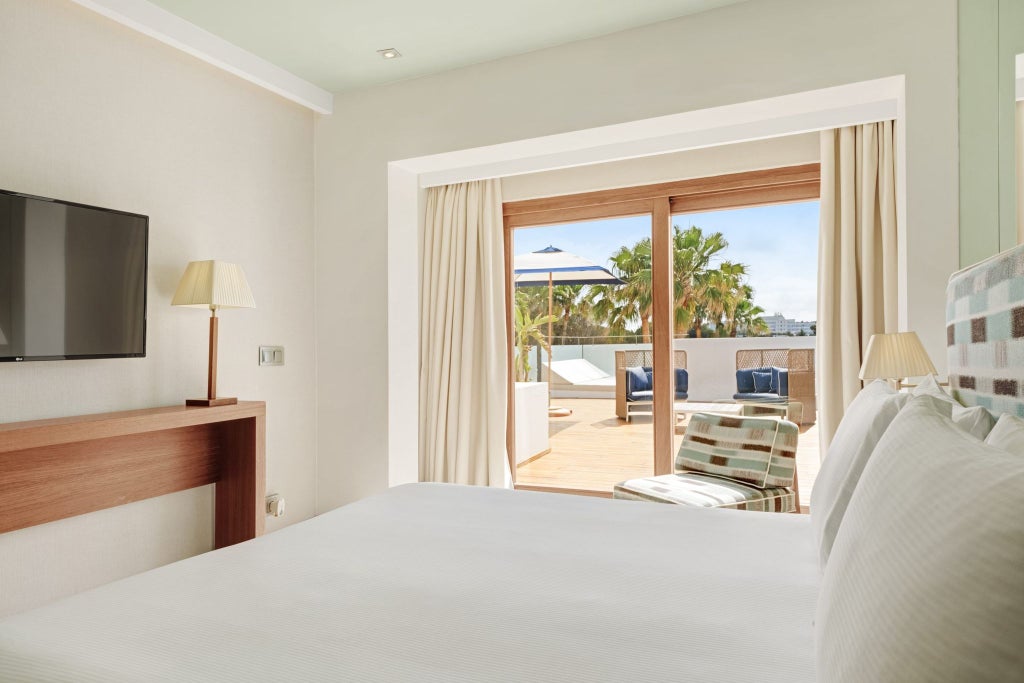 Luxurious beachfront hotel room with minimalist design, crisp white linens, and panoramic sunrise view over Spanish coastline through floor-to-ceiling windows