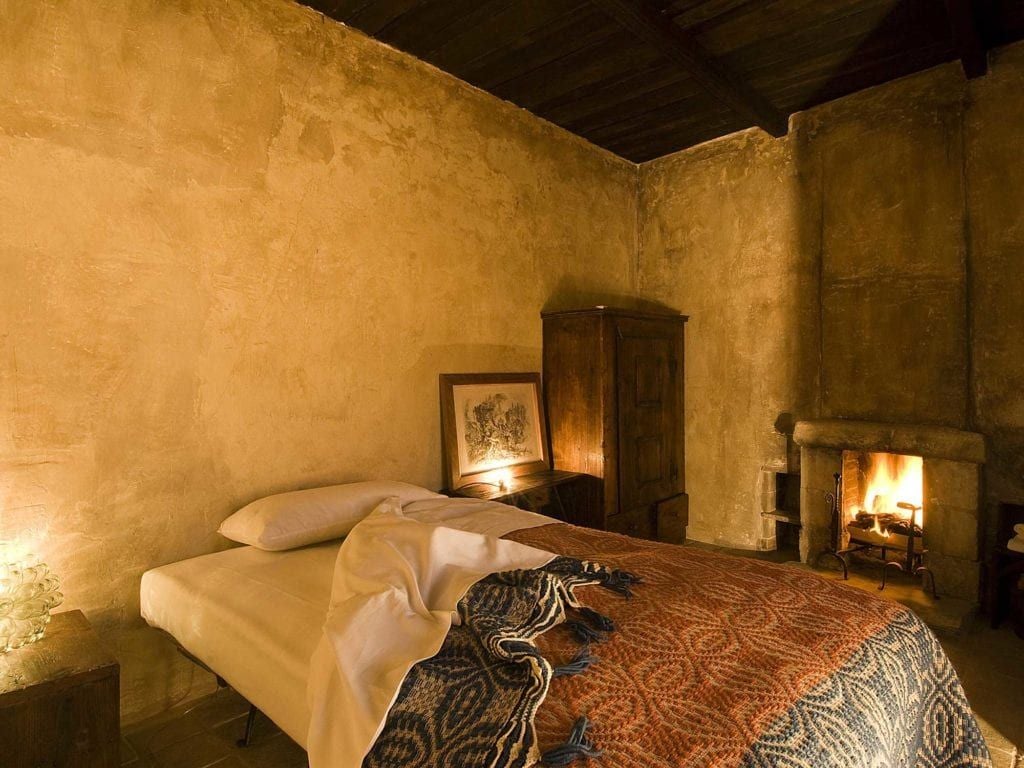 Rustic Italian hotel room with stone walls, wooden ceiling, traditional antique furnishings, and a stunning view of historic church campanile through arched window