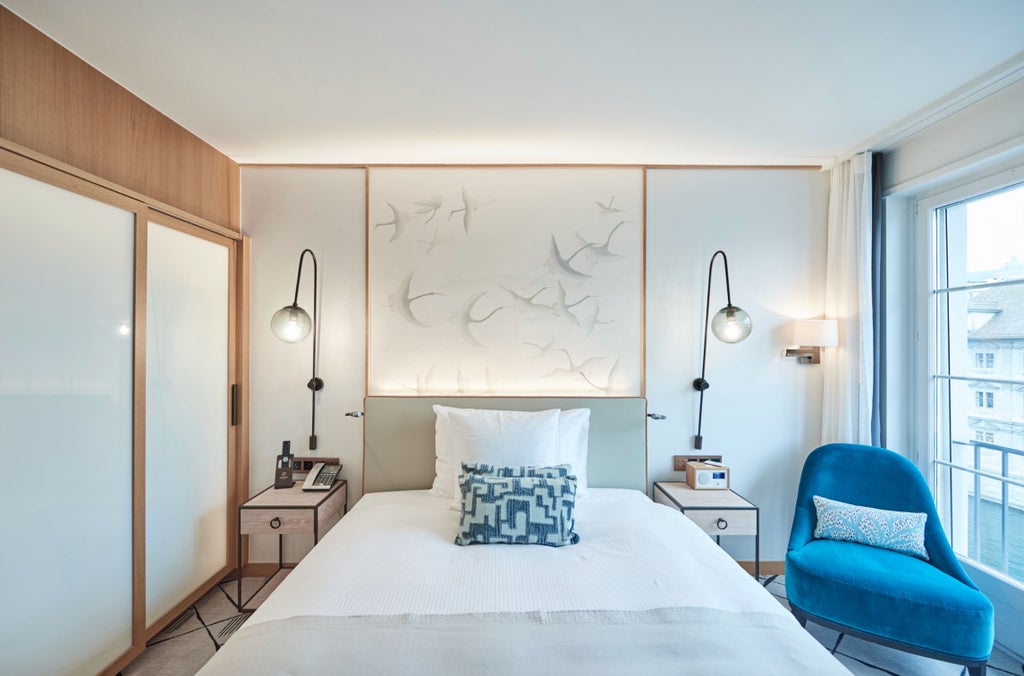 Elegant riverside queen room with panoramic Limmat views, featuring plush white bedding, designer furniture and refined Swiss decor