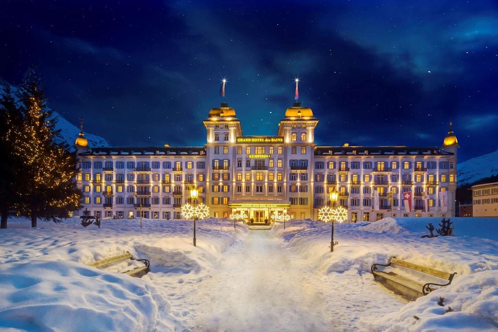 Five-star alpine resort with white facade and balconies nestled against snow-capped mountains, surrounded by manicured gardens