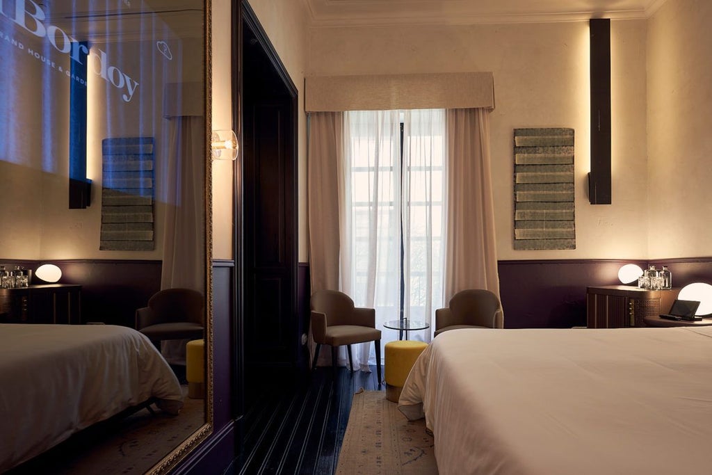 Elegant junior suite with antique wooden furniture, soft white linens, ornate chandelier, and expansive windows overlooking a lush garden at Can Bordoy luxury hotel in Spain.