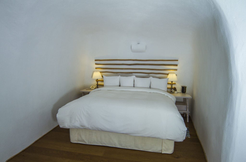 Luxurious white cave-style suite with blue-domed architecture, panoramic Aegean Sea view, elegant minimalist Cycladic design at scenic Santorini hotel