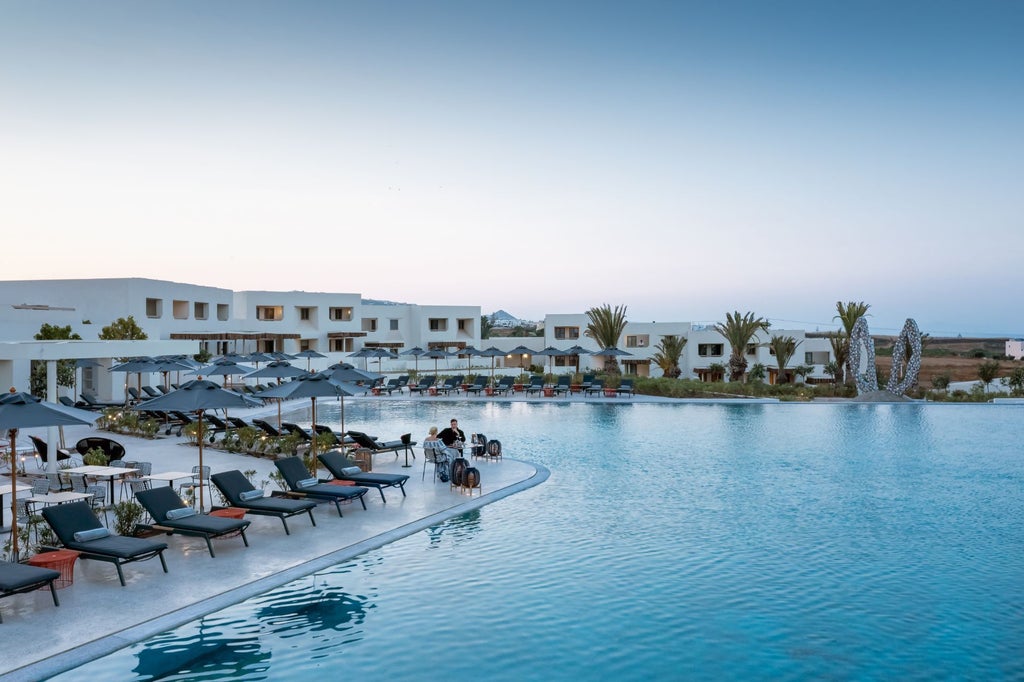 Modern white luxury hotel with minimalist architecture, private balconies and infinity pool overlooking the Mediterranean Sea at sunset