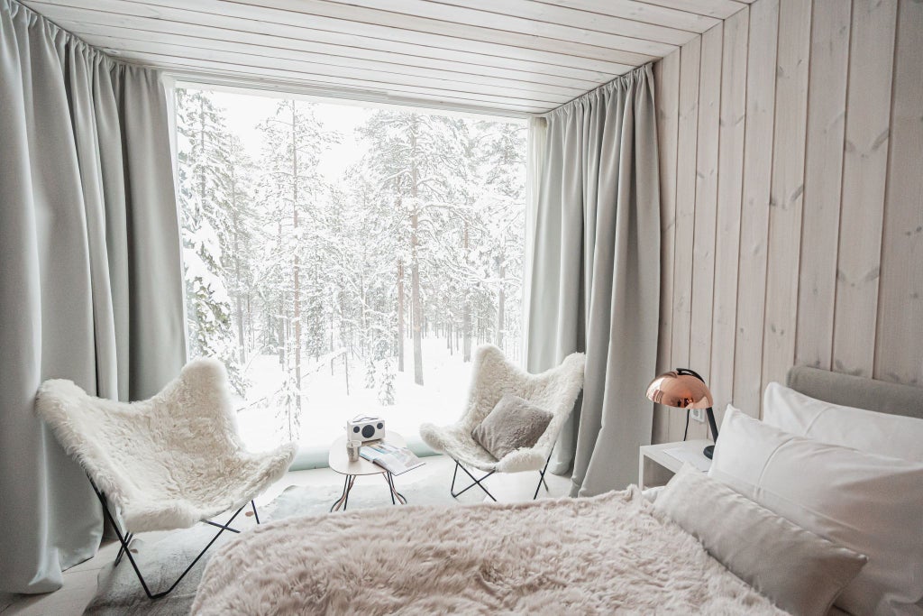 Panoramic Nordic suite with floor-to-ceiling windows overlooking snow-covered forest, modern minimalist design with warm wood accents and cozy luxury interior