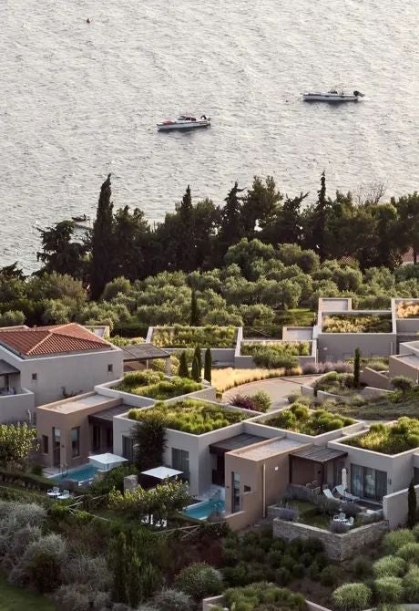 Luxury beachfront villas with private pools overlooking azure Aegean waters, featuring minimalist white architecture and lush Mediterranean landscaping at scenset resort in Greece.