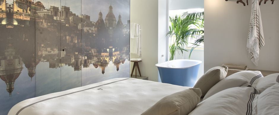 Elegant boutique hotel suite with plush white bed, minimalist design, warm wooden floors, and soft ambient lighting in Malta's historic setting