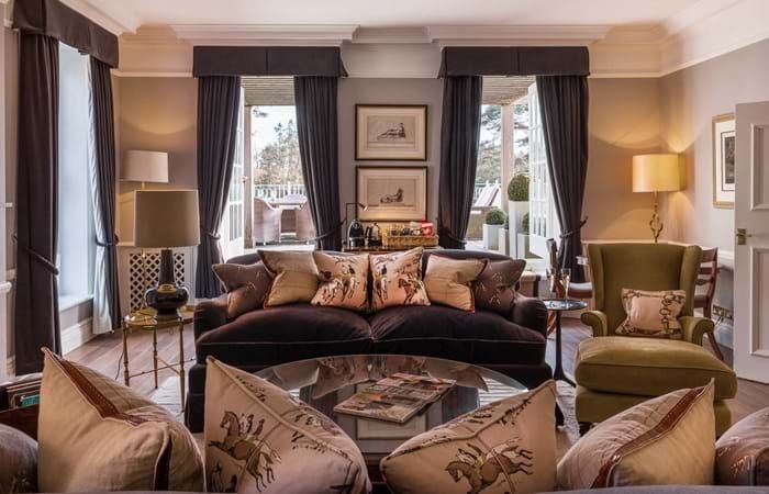 Spacious luxury suite at Chewton Glen Hotel & Spa, featuring elegant wood furnishings, plush white bedding, and large windows showcasing a serene countryside view