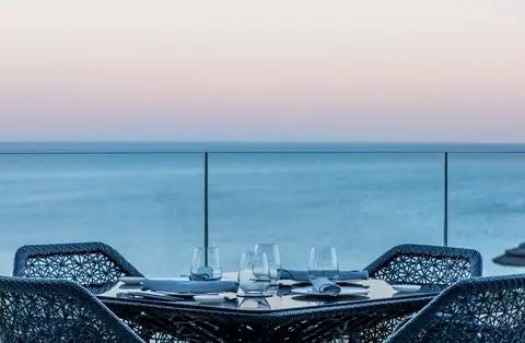 Luxurious coastal resort with infinity pool overlooking azure ocean, lush gardens, and white Mediterranean-style buildings at scenic Portugal destination