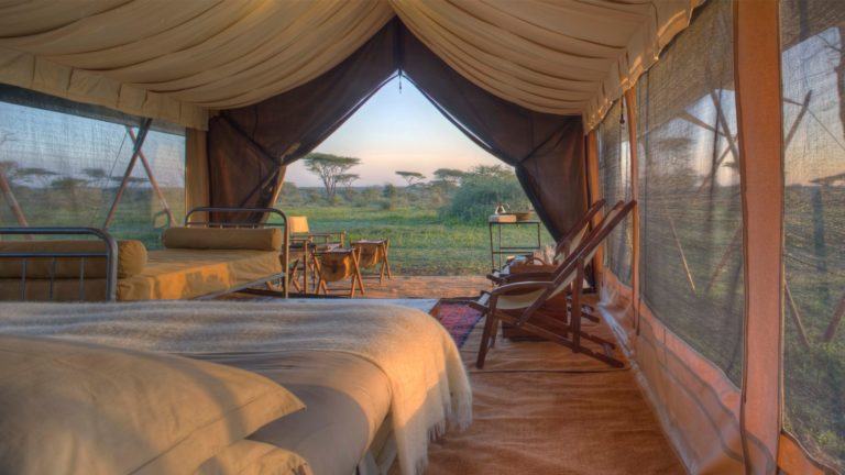 Luxurious safari tent with canvas walls and wooden deck overlooking vast Serengeti plains during golden evening light