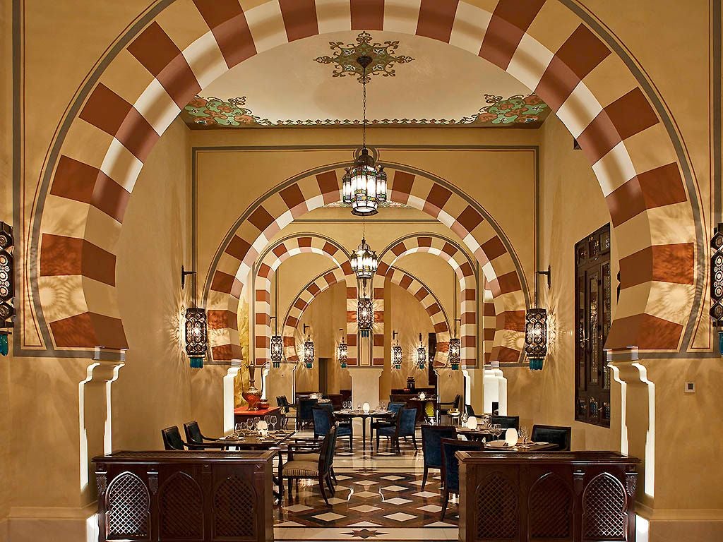 Elegant colonial-era luxury hotel overlooking the Nile River, with ornate Moorish architecture, lush gardens, and stunning sandstone desert landscape backdrop