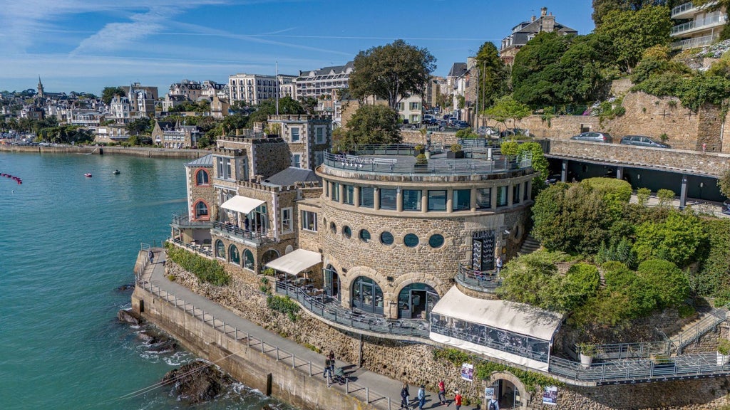 Elegant seaside hotel with blue-gray stone facade nestled on rocky Brittany coastline, luxurious spa windows overlooking dramatic ocean panorama