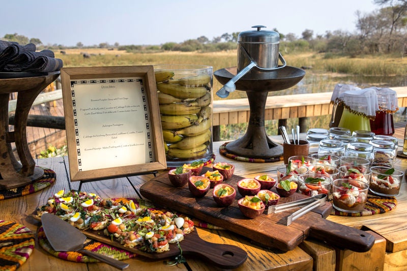 Elevated luxury safari tent with private deck overlooking African savanna, surrounded by acacia trees at sunset in Chobe National Park