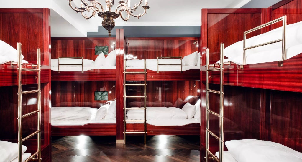 Elegant dormitory-style hotel room at Grand Ferdinand, Vienna, with wooden bunk beds, plush white linens, and warm ambient lighting creating a luxurious alpine retreat atmosphere