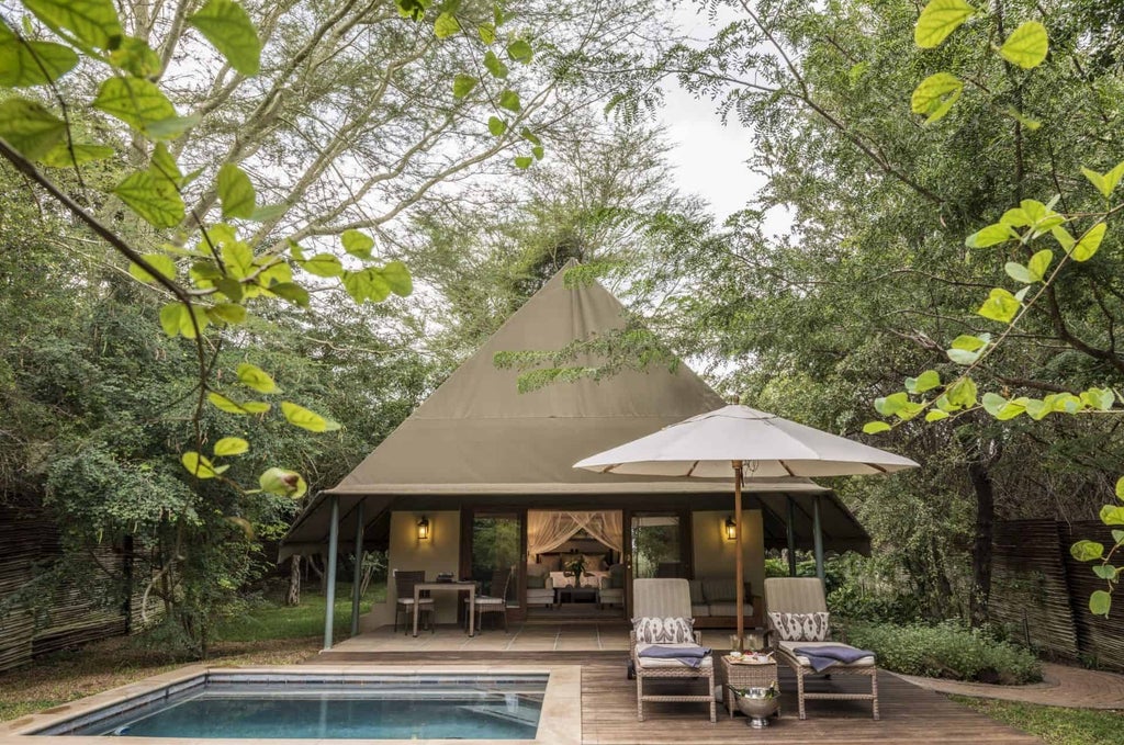 Luxurious African safari lodge with thatched roof overlooking private waterhole, surrounded by savanna grasslands at golden hour