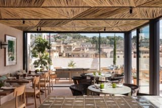 Modern boutique hotel exterior with rustic stone walls, floor-to-ceiling glass windows, and sleek wooden accents in charming Spanish street