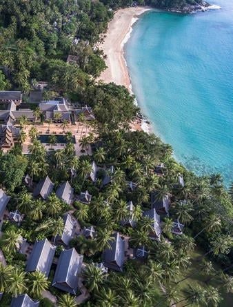 Infinity pool overlooking Andaman Sea at sunset, with traditional Thai-style pavilions nestled among palm trees and tropical gardens