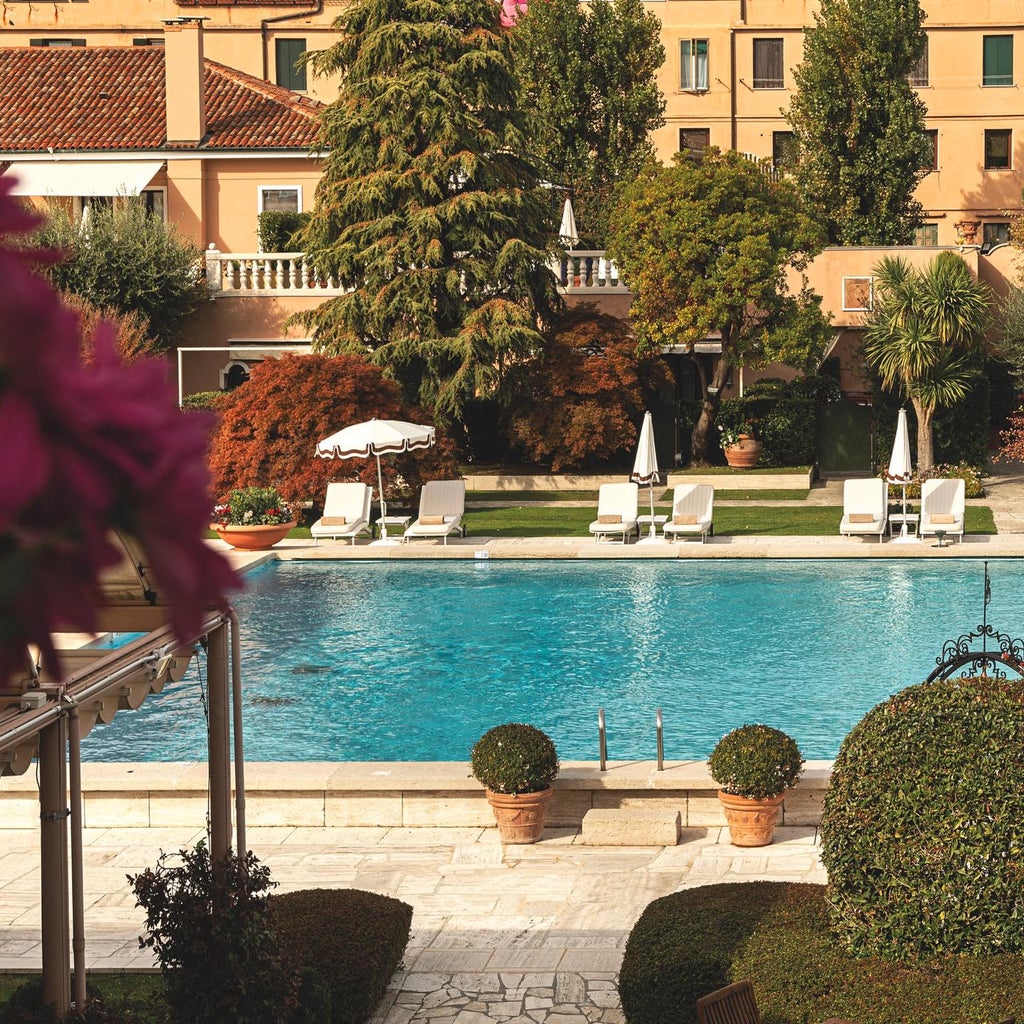 Luxurious Belmond Cipriani Hotel in Venice, Italy, featuring elegant waterfront terrace with white umbrellas overlooking lagoon at sunset