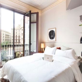 Elegant contemporary hotel room in Barcelona with minimalist design, crisp white linens, city view, and soft natural lighting streaming through large windows