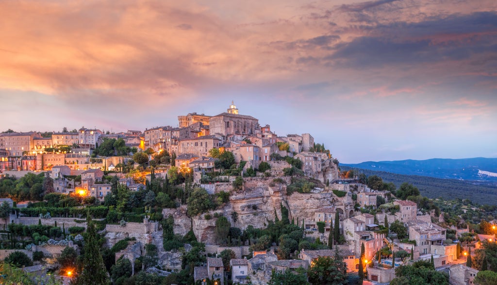 Rustic stone houses with terracotta roofs nestled in Provence's Luberon Valley, surrounded by rolling lavender fields and cypress trees