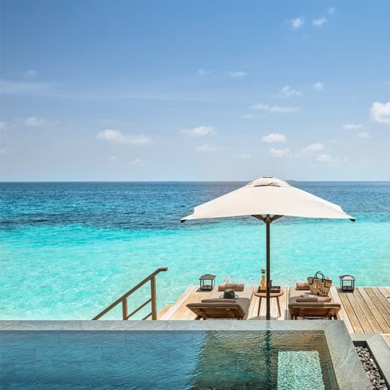 Luxurious overwater villa with private infinity pool stretches over crystal-clear turquoise lagoon in tropical Maldivian paradise