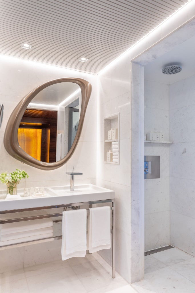 Elegant hotel room with floor-to-ceiling windows overlooking Copacabana Beach, featuring modern Brazilian design, crisp white linens, and warm wood accents