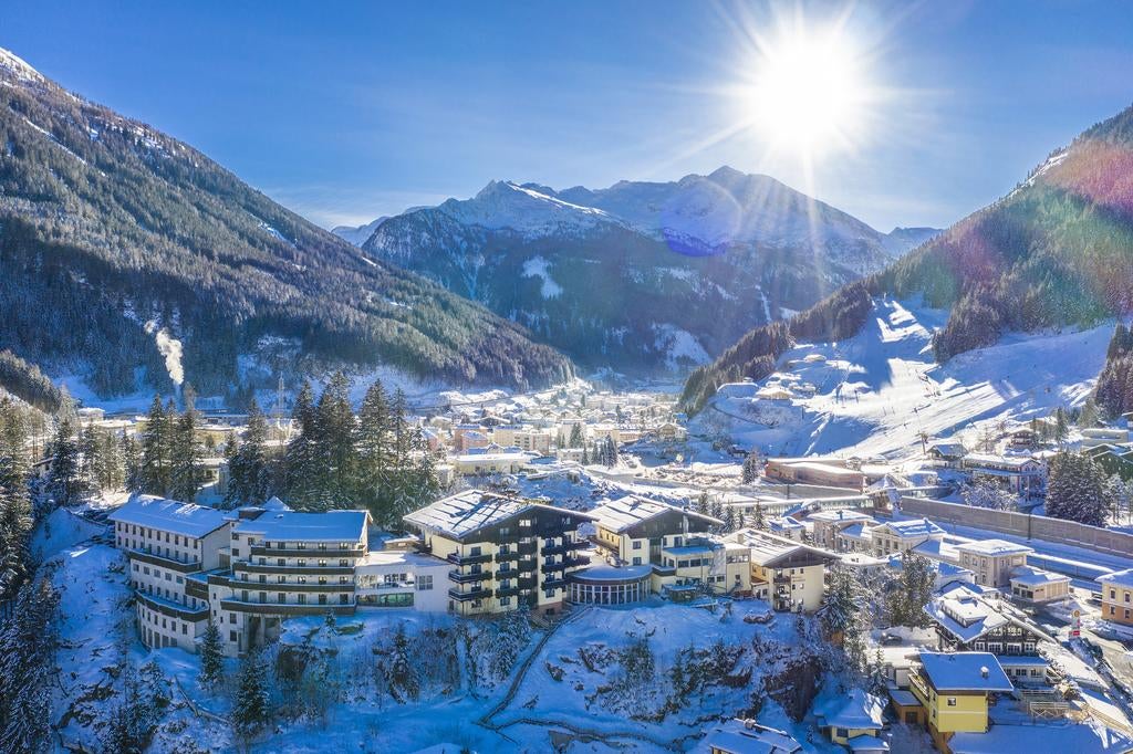 Elegant mountain-view Hotel Miramonte in Austria with modern glass facade, set against snow-capped Alps and surrounded by lush pine forest